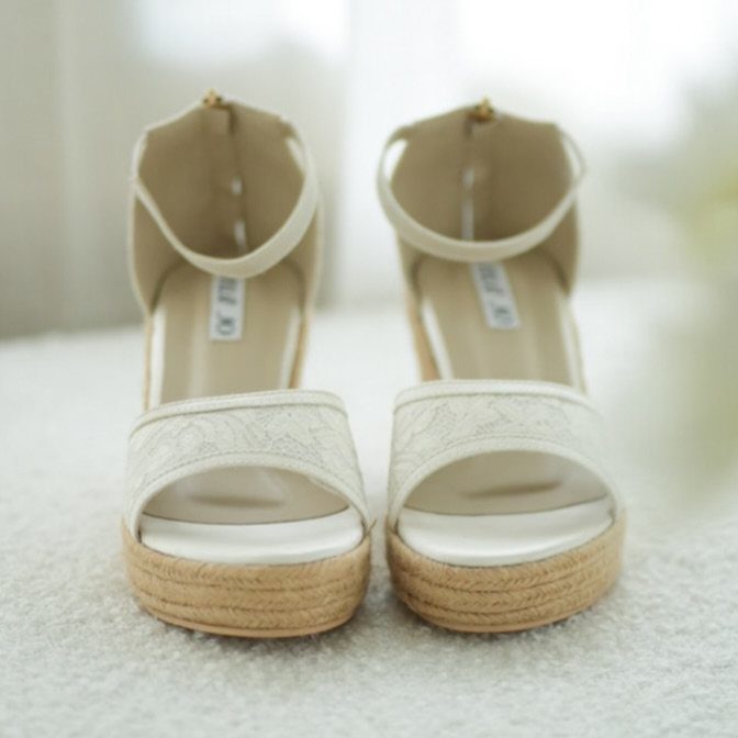 Cream platform wedge sandals with ankle straps and lace detailing on white background