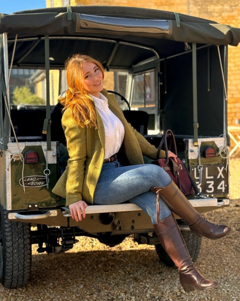 Woman in olive blazer and brown boots sitting on a vintage Land Rover