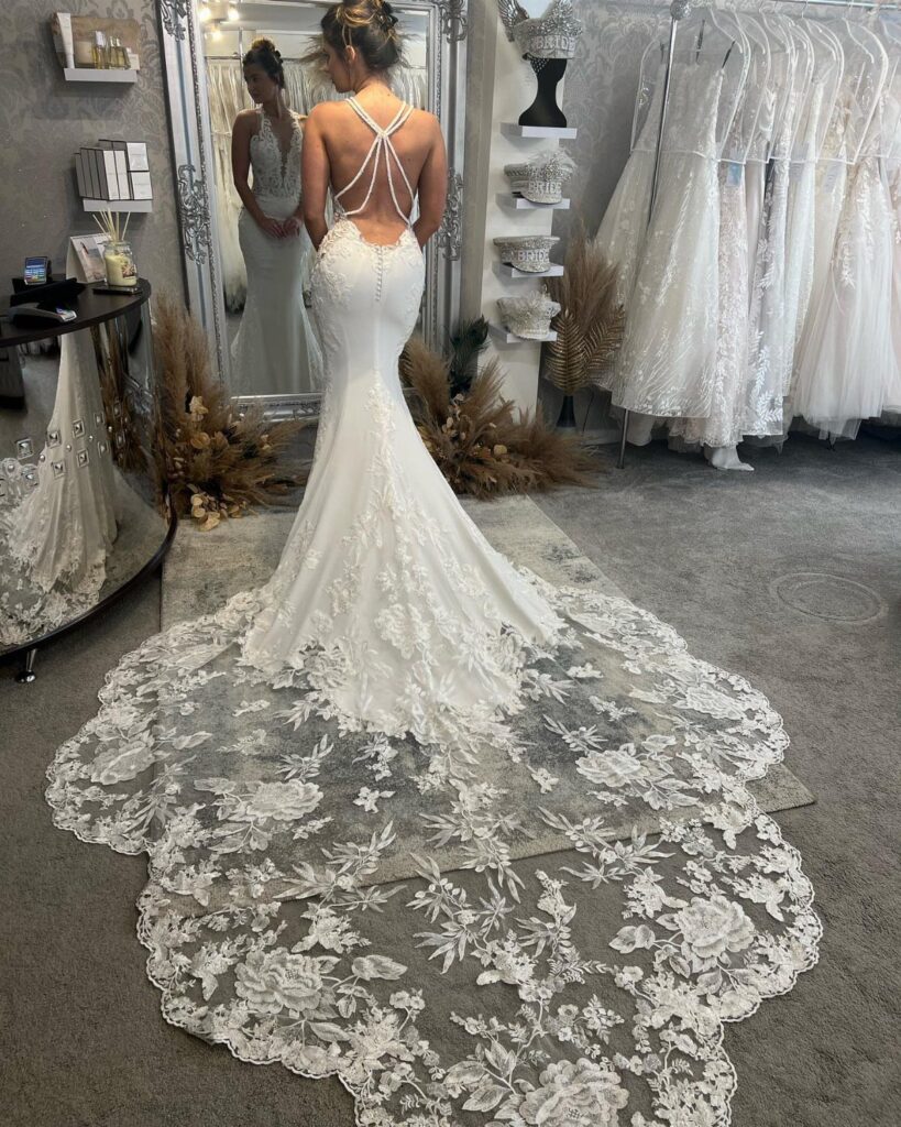 Woman wearing a white backless wedding dress with a long lace train in shop
