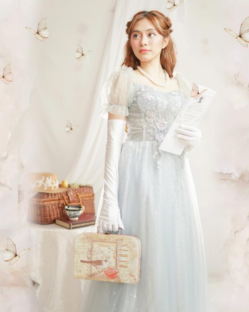 Woman in a light blue Regency gown with white gloves and pearl necklace.