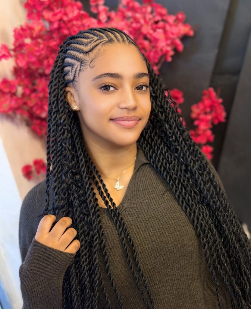 Woman with intricate black cornrow braids and long twists posing before pink flowers