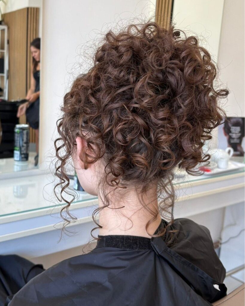 Curly brown hair styled in a voluminous updo seen from behind in salon