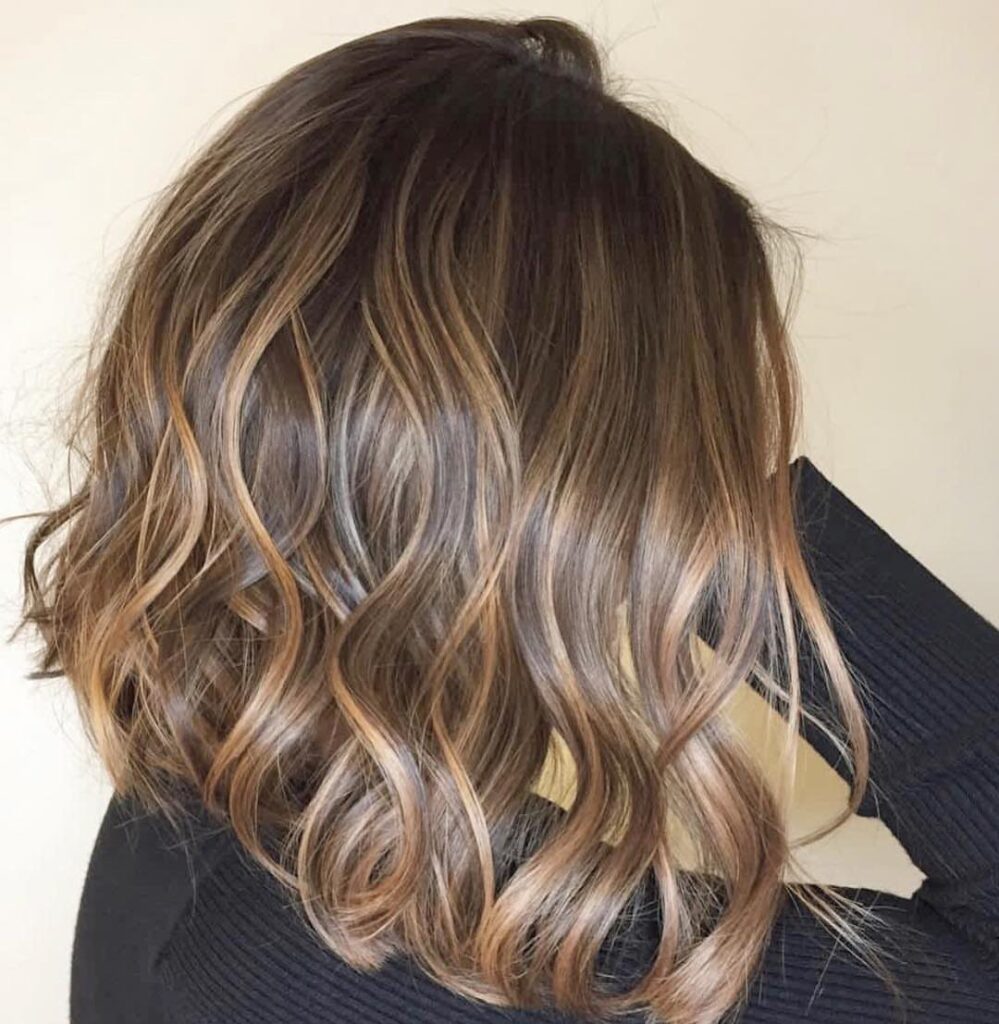 Wavy shoulder-length hair with dark brown roots and honey blond highlights.