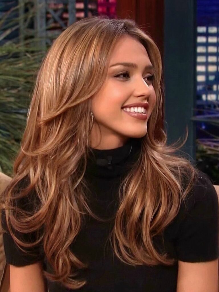 Jessica Alba with long layered honey-blonde hair smiling in a black turtleneck