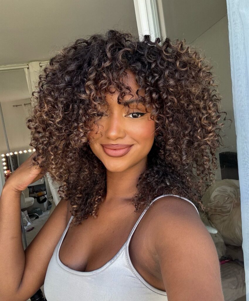 Woman with voluminous brown curly hair and face-framing layers smiling for a portrait.