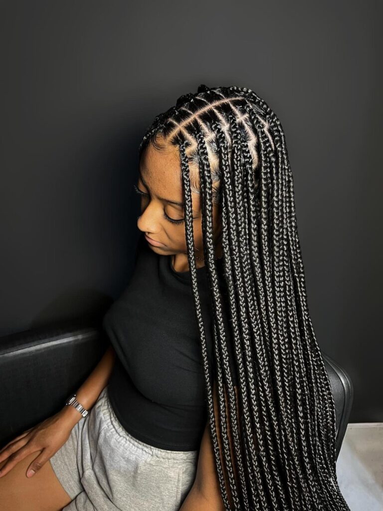 Woman with long black box braids wearing a black t-shirt and grey shorts.