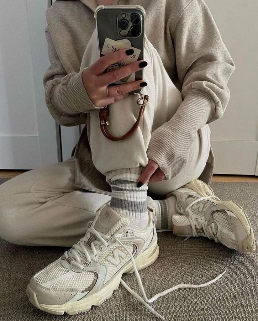 Neutral New Balance sneakers worn with beige loungewear and striped socks in a mirror selfie.