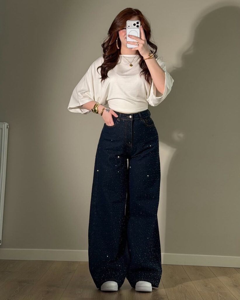 Woman wearing a white blouse and wide-leg dark blue rhinestone embellished denim jeans.
