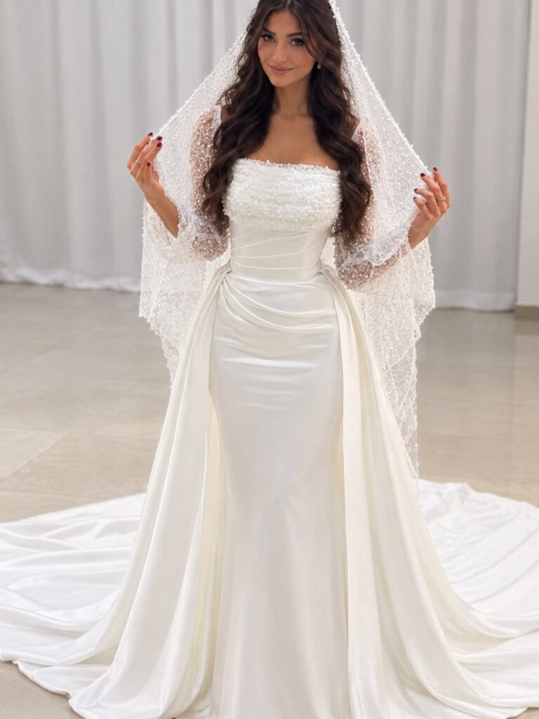 Woman wearing a white beaded wedding dress with a long train and lace veil.