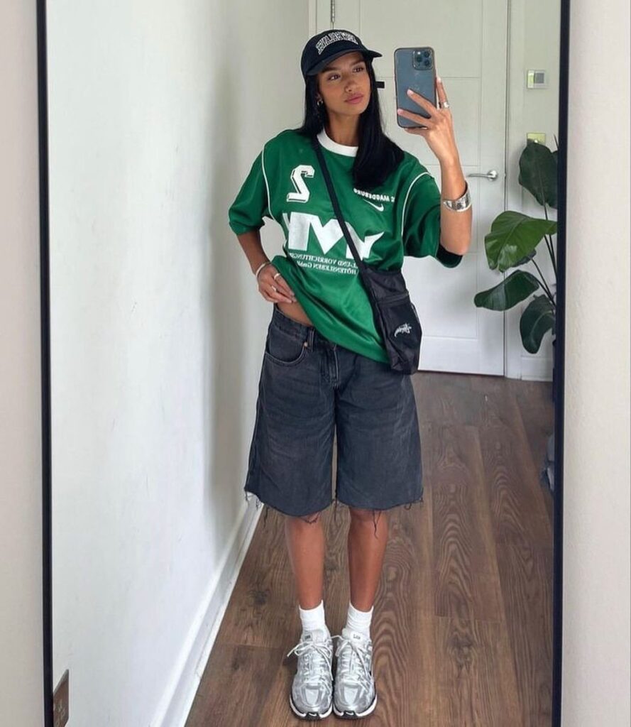 Woman in green graphic tee, black denim shorts, and silver sneakers posing for selfie