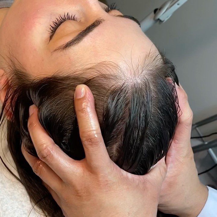 Hands massaging the scalp of a person with dark wet hair and closed eyes