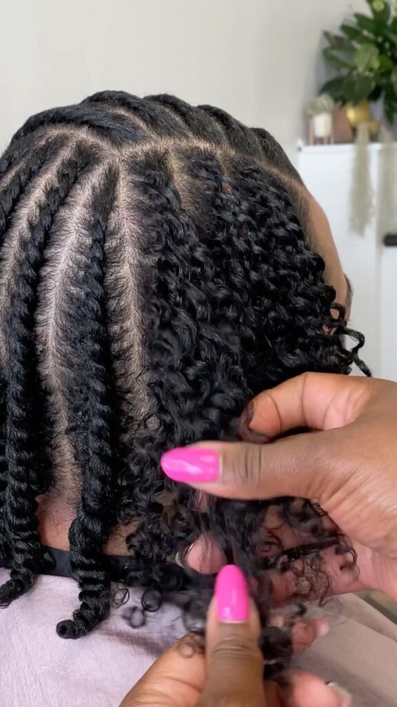 Black 4c hair in defined twists being gently separated by hands with pink nails.