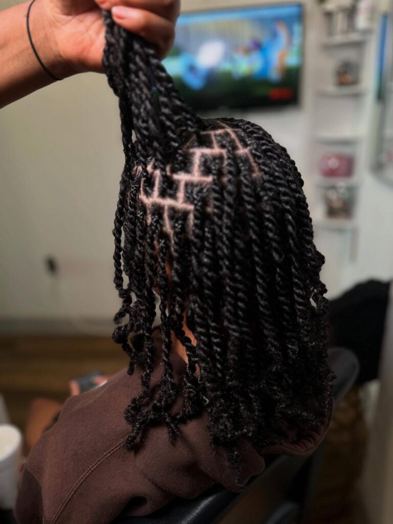 Woman with long black two-strand twists and geometric scalp parting patterns.