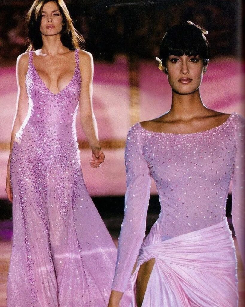 Two models wearing shimmering light purple sequined gowns on a fashion runway.