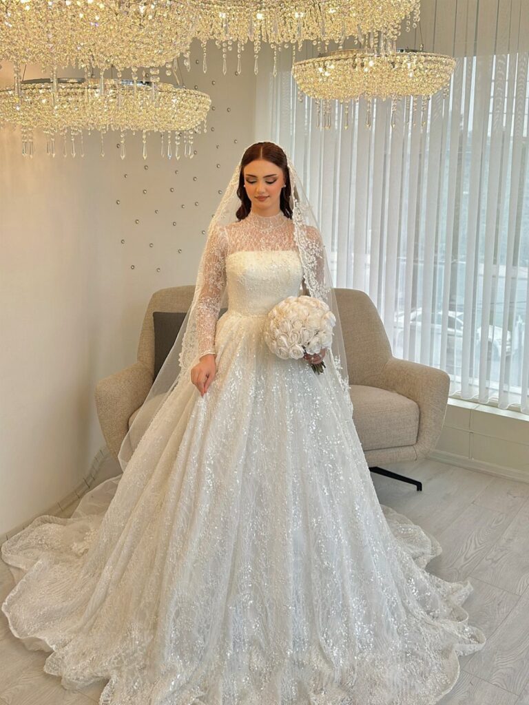 Woman in a sparkling off-white wedding dress with lace sleeves and a veil.