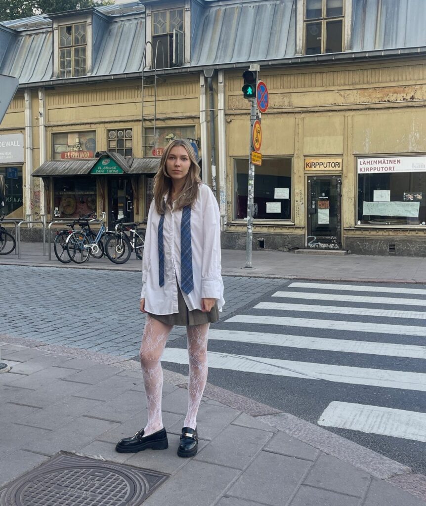 Woman wearing a white shirt, olive green skirt, and patterned tights on a street